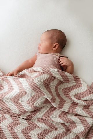 Sleeping baby wearing a pink romper with a pink and cream stripe knitted blanket