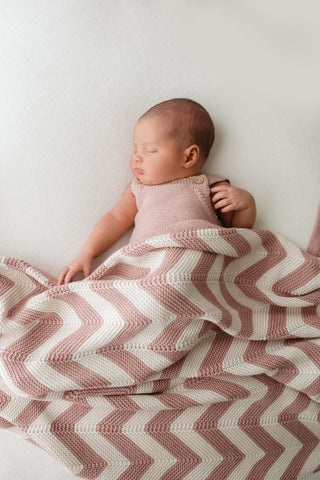 Sleeping baby wearing a pink romper with a pink and cream stripe knitted blanket