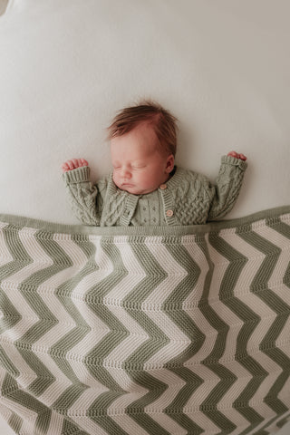 Baby sleeping under a stripe chevron knit blanket in cream and sage green