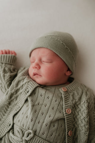 Sleeping baby wearing sage green knit hat, bodysuit and cardigan
