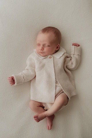 Sleeping baby wearing knitted frill collar cardigan and bloomers