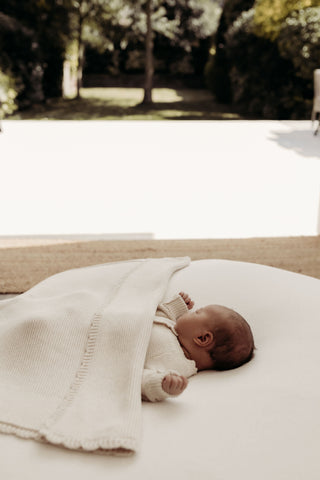 Baby sleeping on a beanbag with a blanket next to a garden in summer 