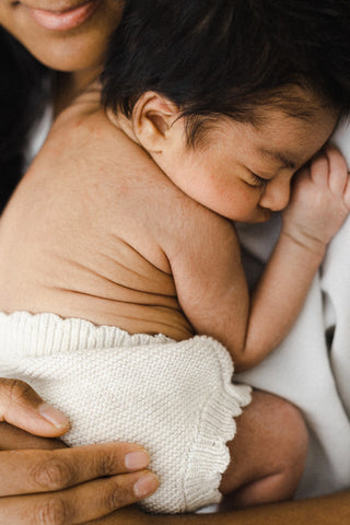 Sleeping newborn baby in mum's arms wearing knitted baby bloomers with a scalloped edge