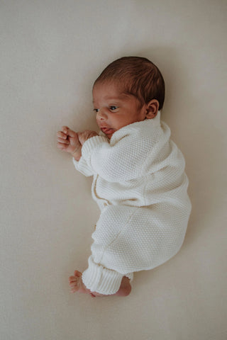 Newborn baby on side wearing knitted white romper