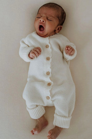 Yawning Baby wearing white knitted romper with buttons