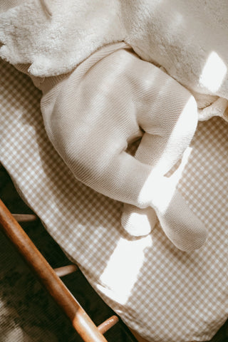 Baby in cot on gingham sheet wearing knitted baby trousers
