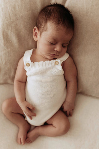 Sleeping baby leaning on a cushion wearing a white knitted romper