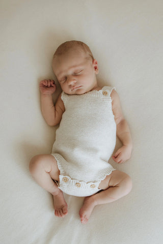 sleeping newborn baby wearing neutral knitted baby onesie