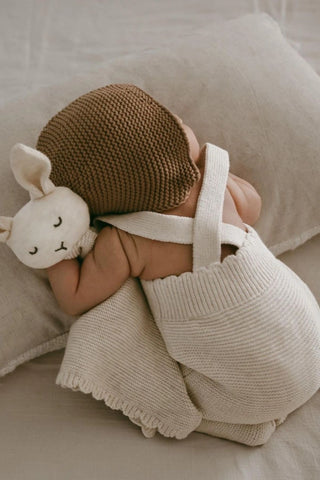 Newborn baby wearing knitted dungarees cuddling a knitted bunny comforter