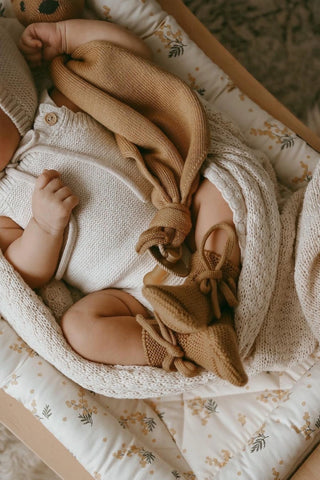Baby in a rocker wearing a knitted romper and booties, wrapped in a blanket