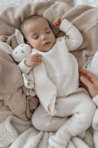 Sleeping Baby lying on blankets, wearing a knitted outfit, cuddling a bunny comforter