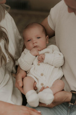 Baby being carried wearing neutral ribbed baby romper and booties