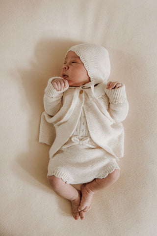 Newborn baby wearing knitted bonnet, cardigan, and bloomers