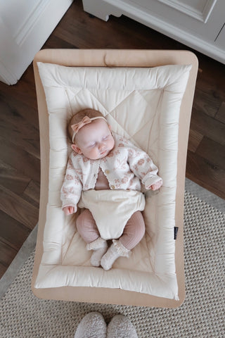 Baby asleep in chair wearing pink bow headband and knitted pink outfit