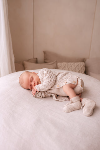 Baby sleeping on a beanbag with cushions behind wearing a neutral knitted outfit