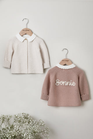 Pair of knitted Baby Cardigans on Isla & Fraser hangers, one in beige and one in pink with 'Bonnie' name embroidery. 
