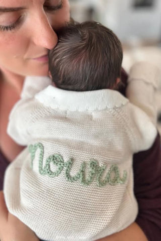 Mother cudding newborn baby wearing named embroidered cardigan