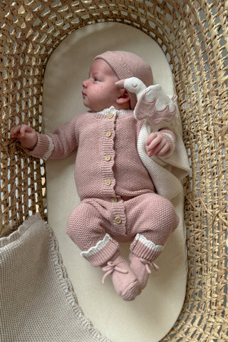 Baby in Moses Basket in knitted pink outfit cuddling stork comforter