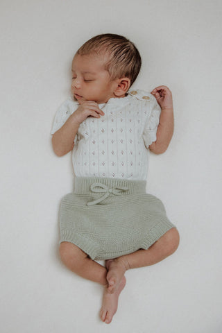 Sleeping newborn baby in knitted pointelle bodysuit and sage green bloomers