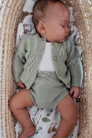 Baby sleeping in moses basket wearing knitted sage cardigan and bloomers