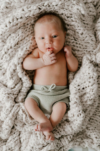 Newborn baby in chunky knit blanket wearing sage green knitted baby bloomers