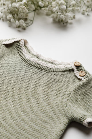 Knitted green baby bodysuit with cream scalloped neckline and wooden buttons