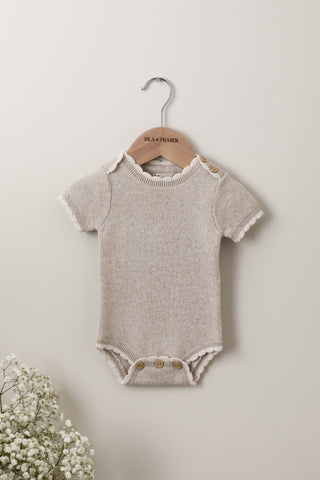 Neutral knitted baby bodysuit with scalloped edging on an Isla & Fraser wooden hander