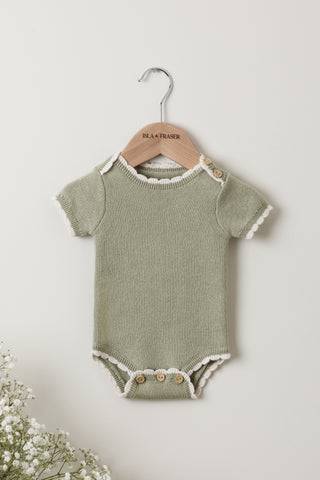 Green baby bodysuit with cream scalloped edging, on an Isla & Fraser wooden hanger