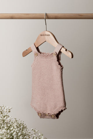 Knitted Pink Baby Romper on a wooden rail on a wooden Isla & Fraser hanger with flowers