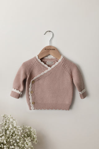 Pink Knitted Wrap Baby Cardigan with a cream scalloped edge on an Isla & Fraser hanger