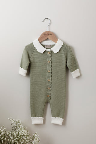 Green knitted baby romper with contrast white collar and cuffs on a wooden Isla & Fraser hanger