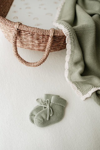 Moses basket with sage blanket with cream scalloped trim, and sage bow booties 
