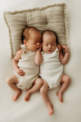 Baby twins with a cushion wearing neutral baby rompers