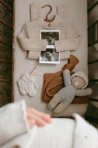 Cot with pregnancy scan and newborn items including a romper, a doll, and Knitted Bow Booties